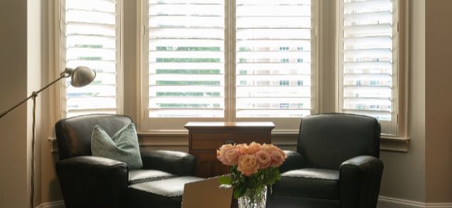 A Seating Area With Chairs Near Windows That Have White Interior Shutters.
